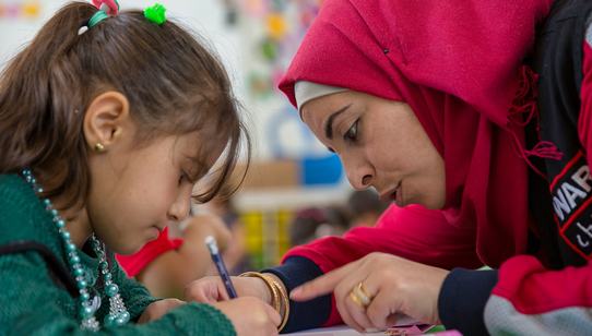 War Child medewerker in Jordanië met War Child-logo helpt kind lezen_War Child Jordanië_180424